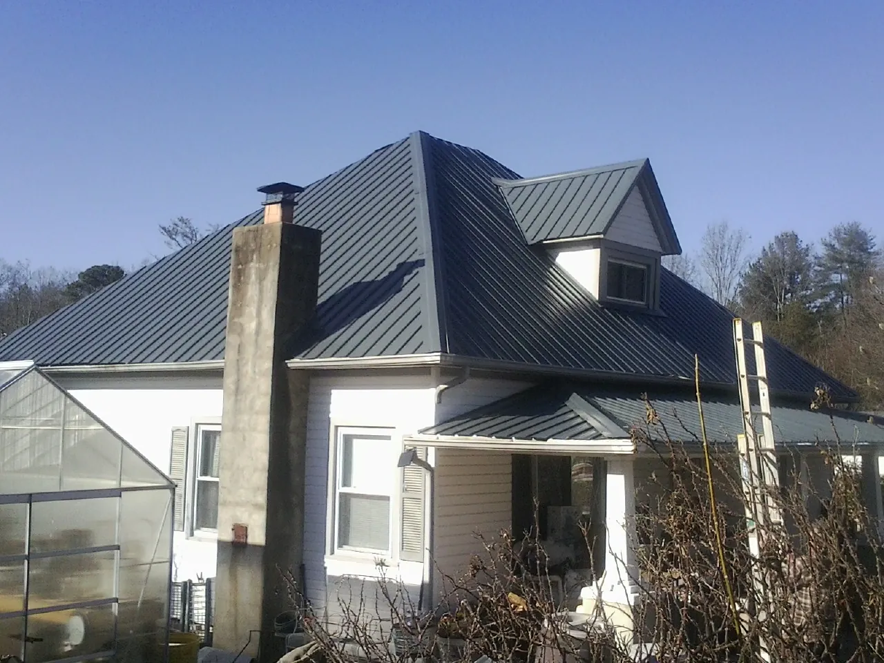 Dark blue standing seam metal roof on a white farmhouse with dormer — Slate & Tile Roof Repair by Roofing Brothers in De Leon Springs