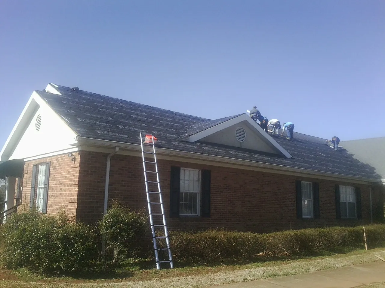 Crew tearing shingles off a brick ranch roof with a ladder set — Emergency Roof Repair work by our crew in De Leon Springs