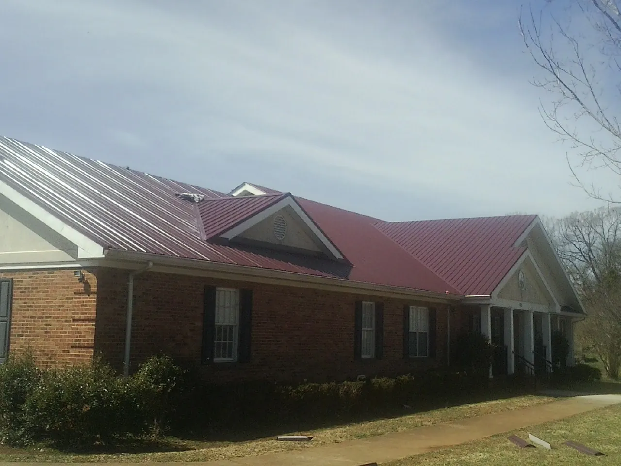 Red metal roof with gabled entries on a long brick building, from a Hail Damage Roof Repair job in De Leon Springs