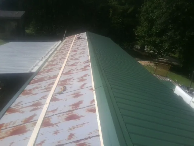 Old rusted panels beside newly installed green metal roofing — Wind Damage Roof Repair by Roofing Brothers in De Leon Springs