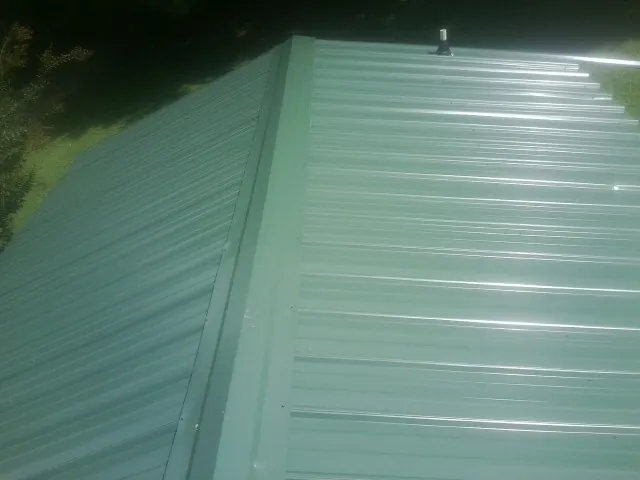 New green metal panels meeting at the ridge of a roof — Flat Roof Repair work by our crew in De Leon Springs