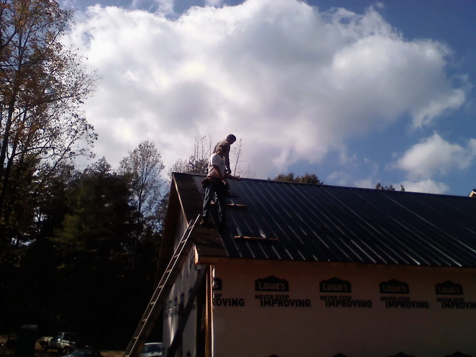 Roofer fastening dark metal panels high against a cloudy sky, from a Roof Inspection job in De Leon Springs