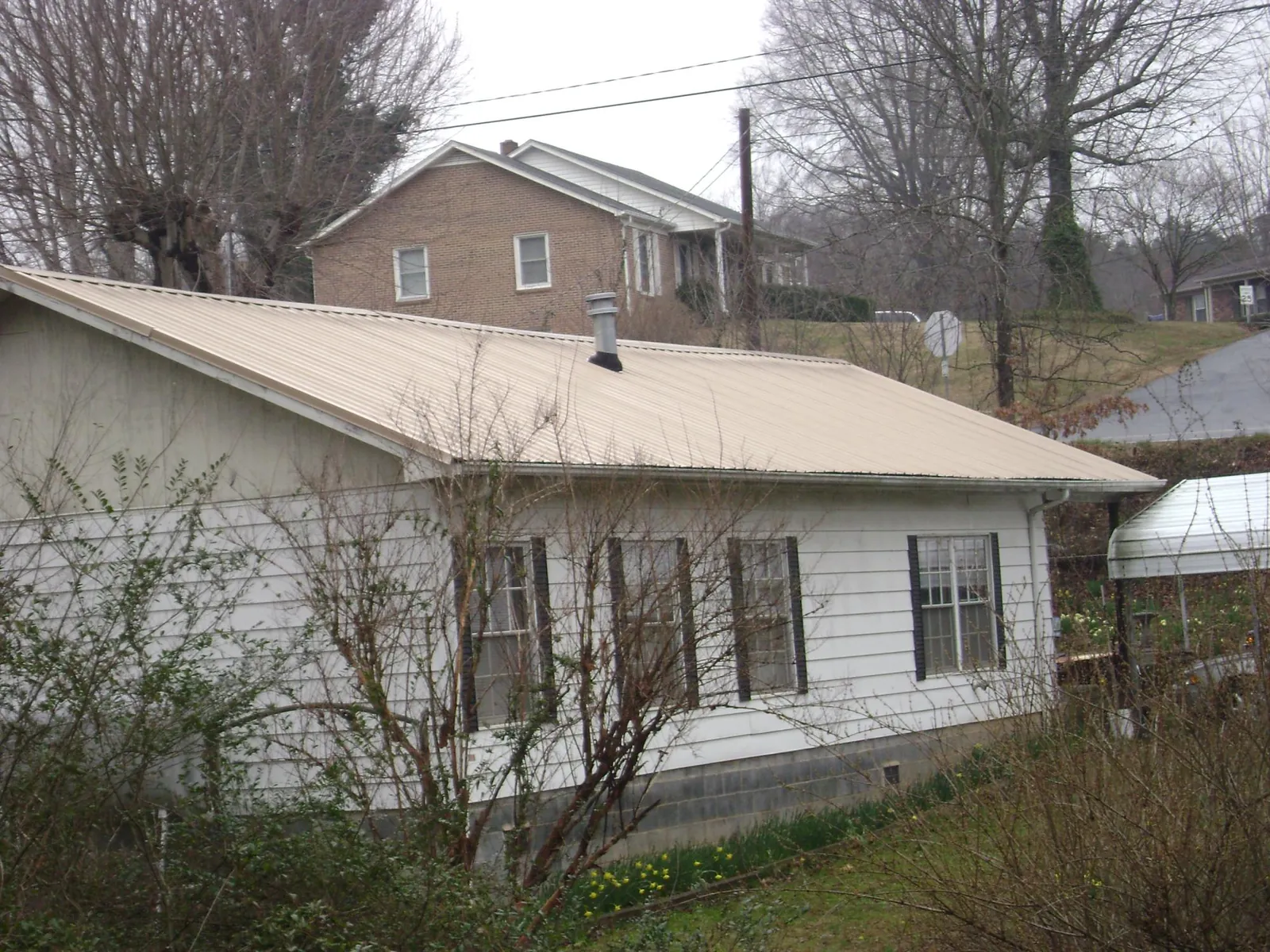 Tan metal roof on a white sided house set into a hillside — Commercial Roofing by Roofing Brothers in De Leon Springs